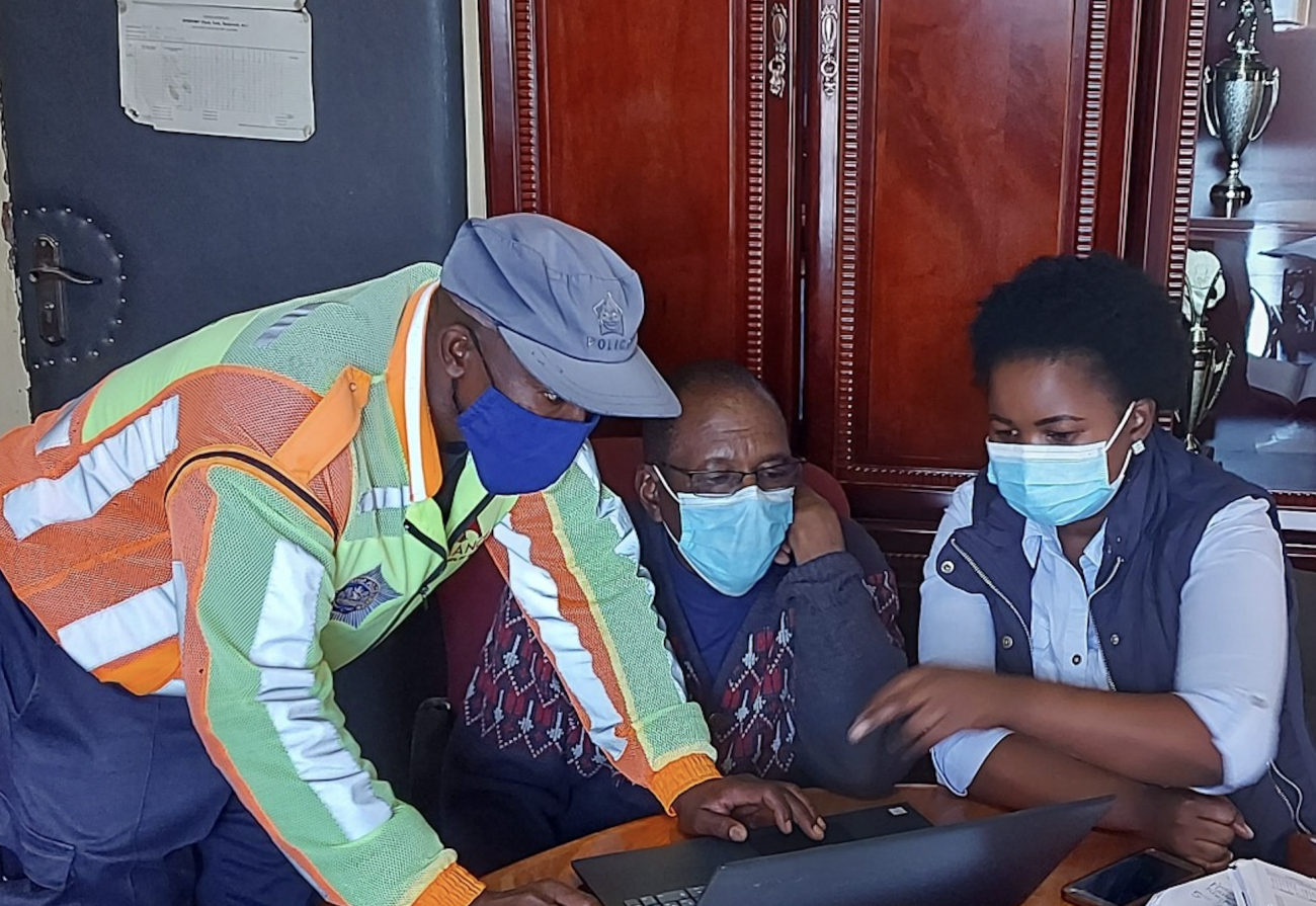 Deux hommes et une femme travaillent autour d’une même table devant un ordinateur portable. Tous trois portent un masque de protection. La femme et un des deux hommes sont assis, tandis que le deuxième homme est debout, penché sur l’ordinateur.