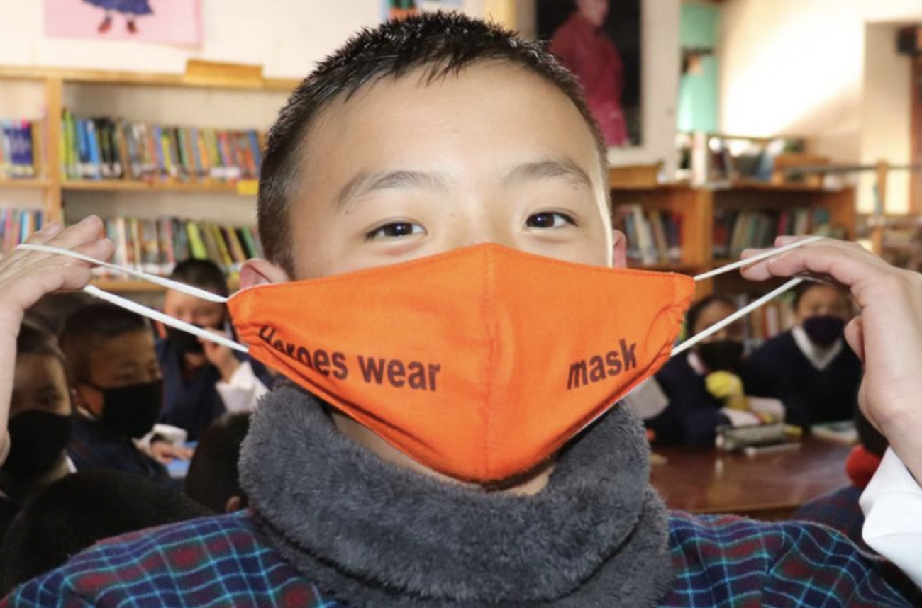 A young boy puts on his orange face mask while looking straight at the camera. 