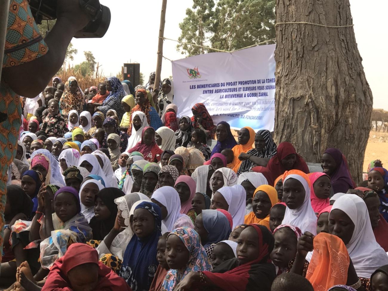 تقف مجموعة كبيرة أمام لافتة بيضاء كبيرة عليها كلمات بالفرنسية.