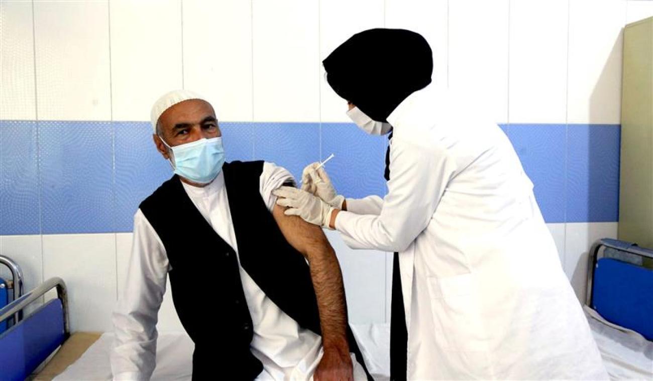 A man sitting down is being vaccinated by a woman standing up in a doctor's office.
