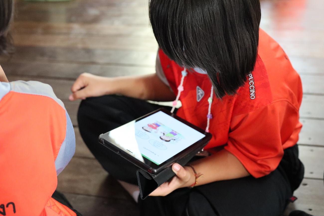 Dos pequeños se sientan uno cerca del otro en el suelo. Un niño mira una tableta.