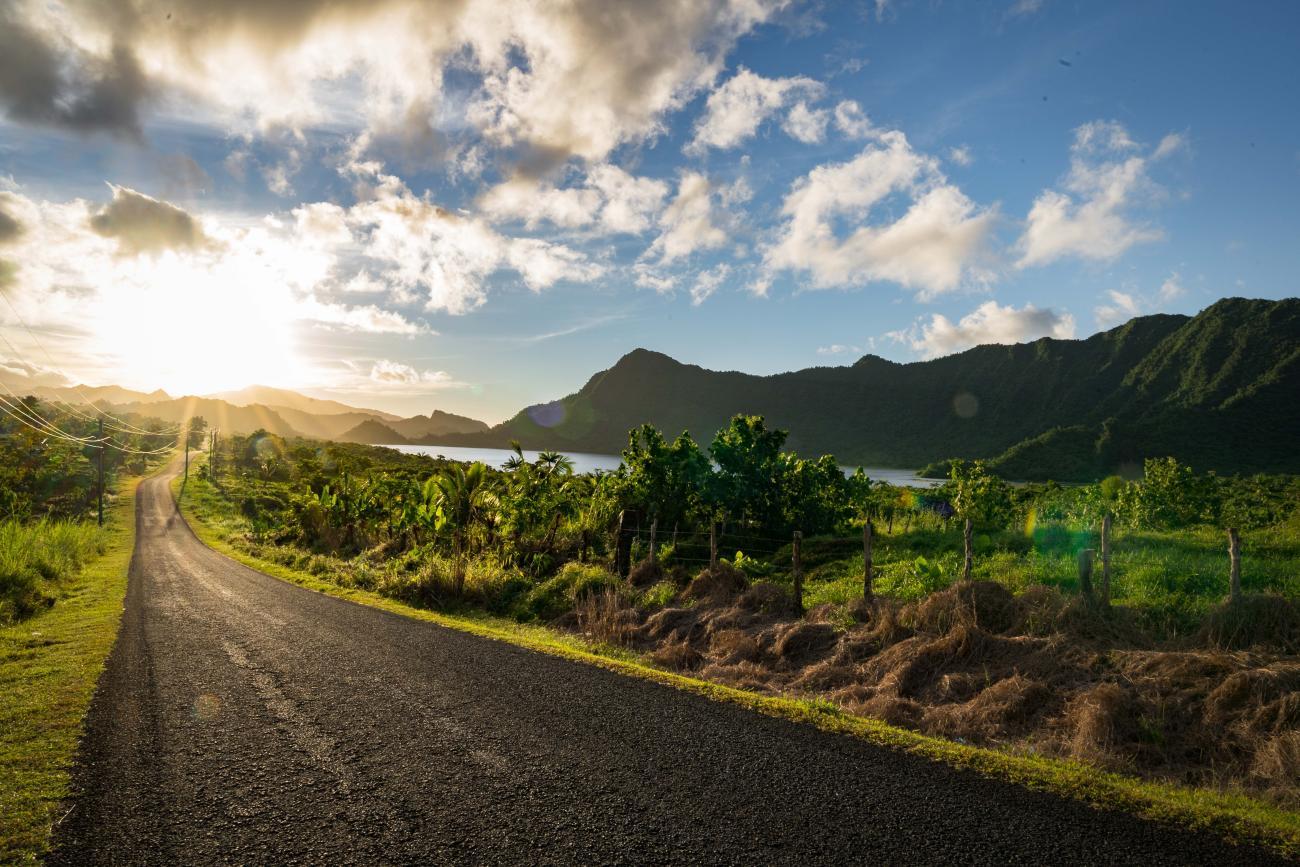 Un hermoso amanecer sobre una carretera, árboles, montañas y agua en la distancia.