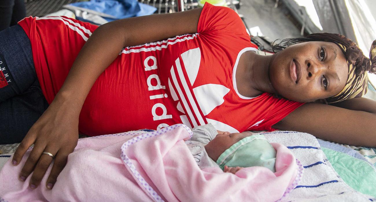 Una madre se tumba en una cama junto a su bebé recién nacido, que está envuelto en una manta rosa.