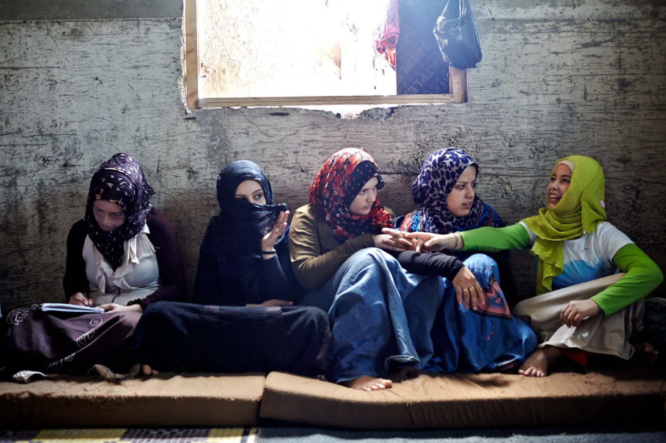 تجلس خمس فتيات معًا يتحدثن ويكتبن أمام الحائط.