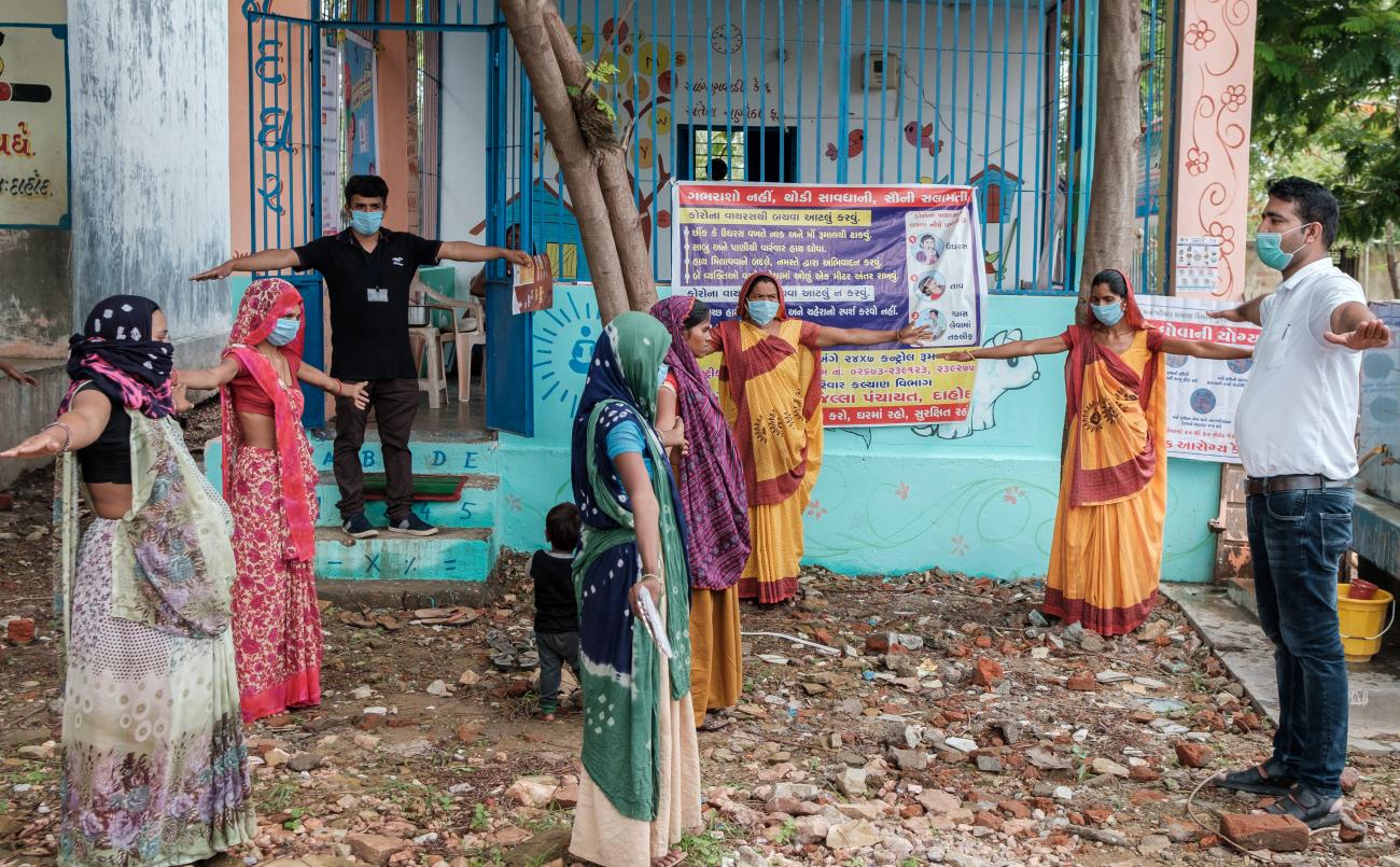 Группа людей стоят с расставленными в стороны руками, практикуя социальное дистанцирование.