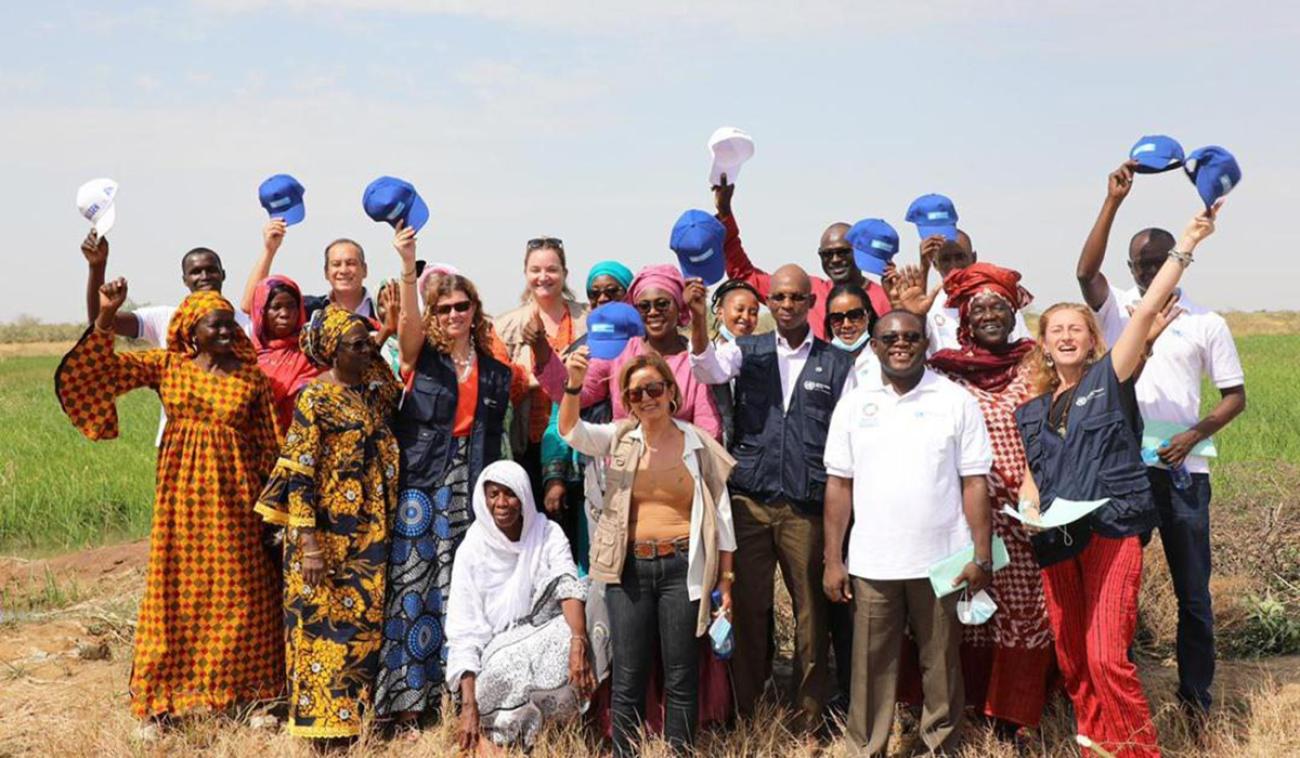 Men and women joyfully raise their arms and hats in the air as they stand together on a green field.