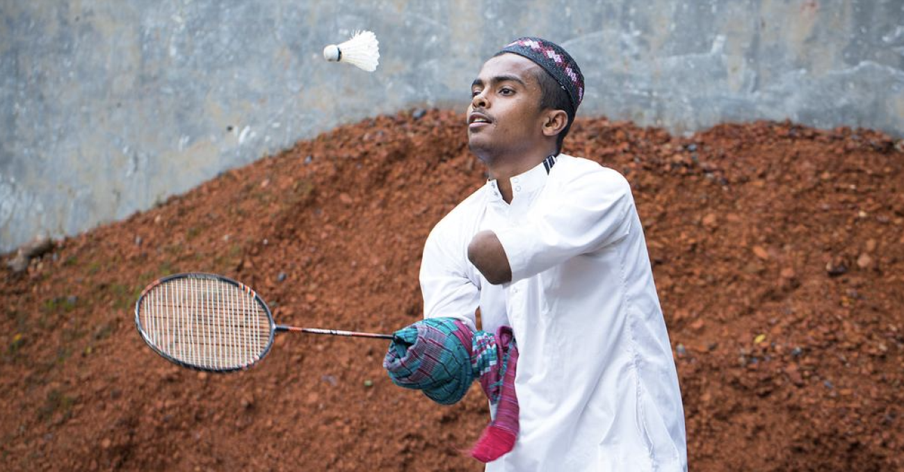 شاب من ذوي الإعاقة يلعب بالريشة الطائرة في الهواء الطلق.