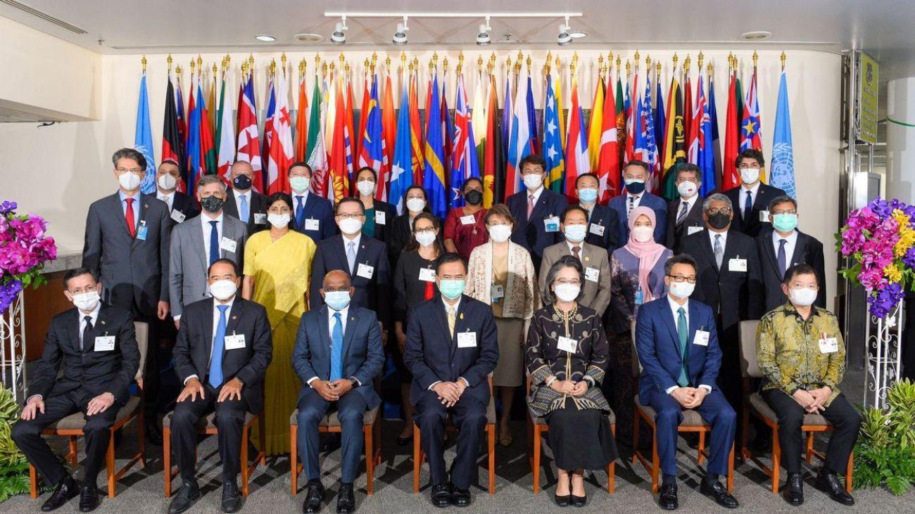 Un groupe de hauts fonctionnaires portant tous un masque de protection respiratoire posent pour une photo devant plsuieurs drapeaux.