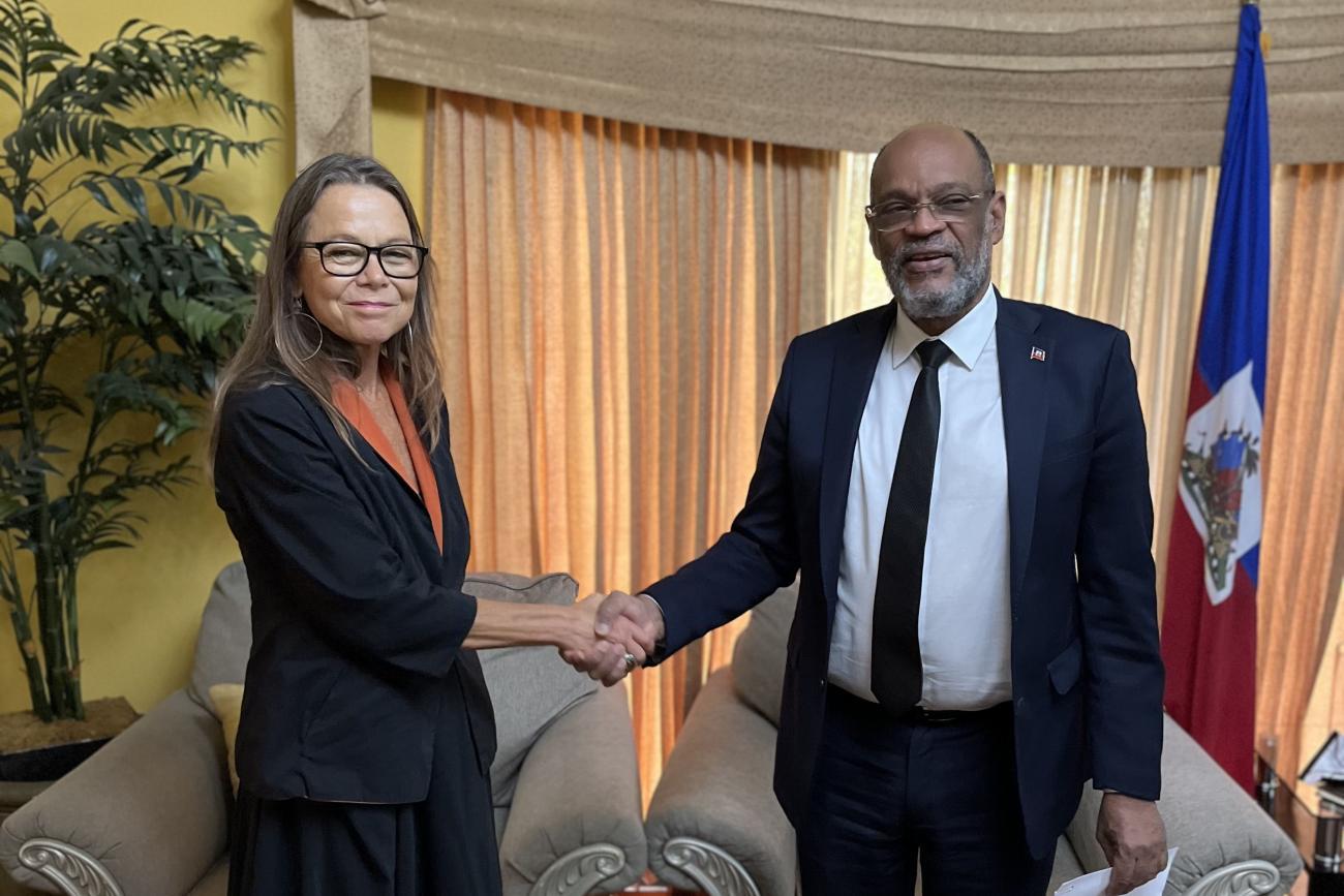Ulrika Richardson, nueva Representante Especial Adjunta de las Naciones Unidas en Haití, y el Primer Ministro haitiano, Ariel Henry, se dan la mano en un despacho con la bandera de Haití como fondo.