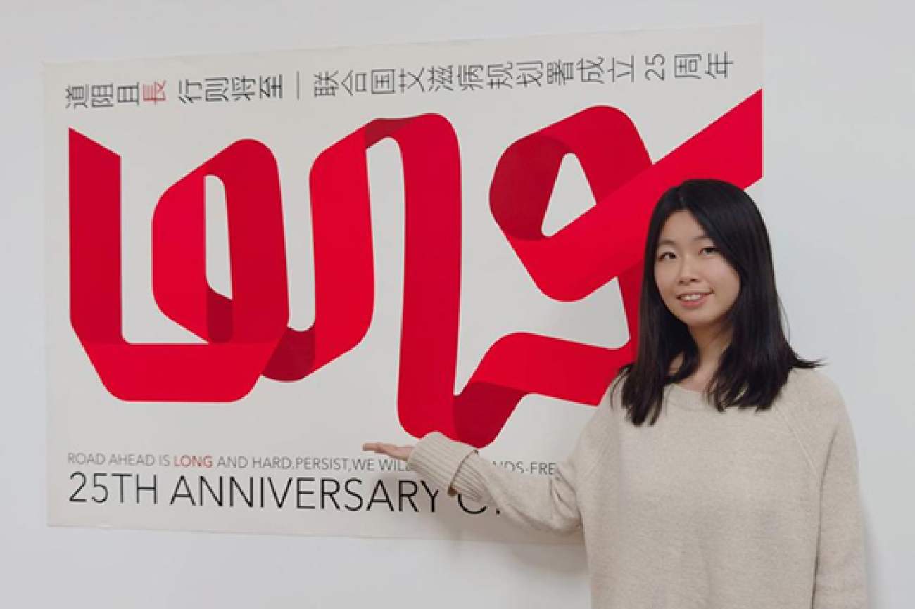 Una joven de China frente a un cartel de un lazo rojo.