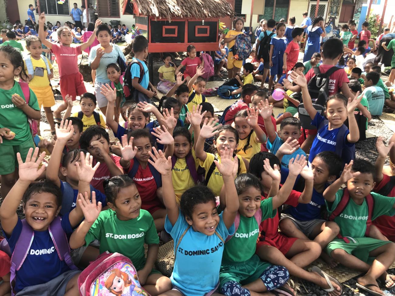 أطفال يرتدون ملابس ملونة يرفعون أيديهم في الهواء.