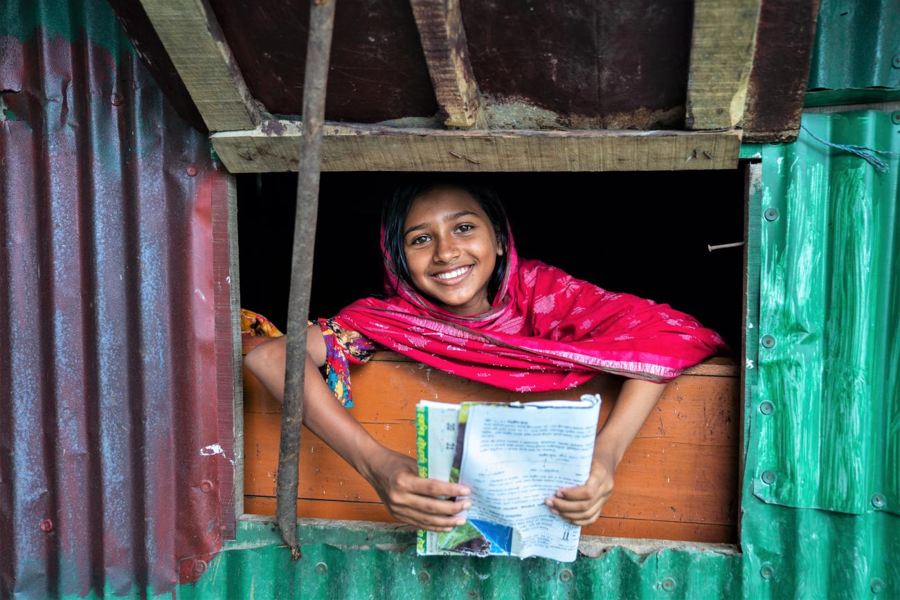 Girl in a pink dress holding a book peeping through a window