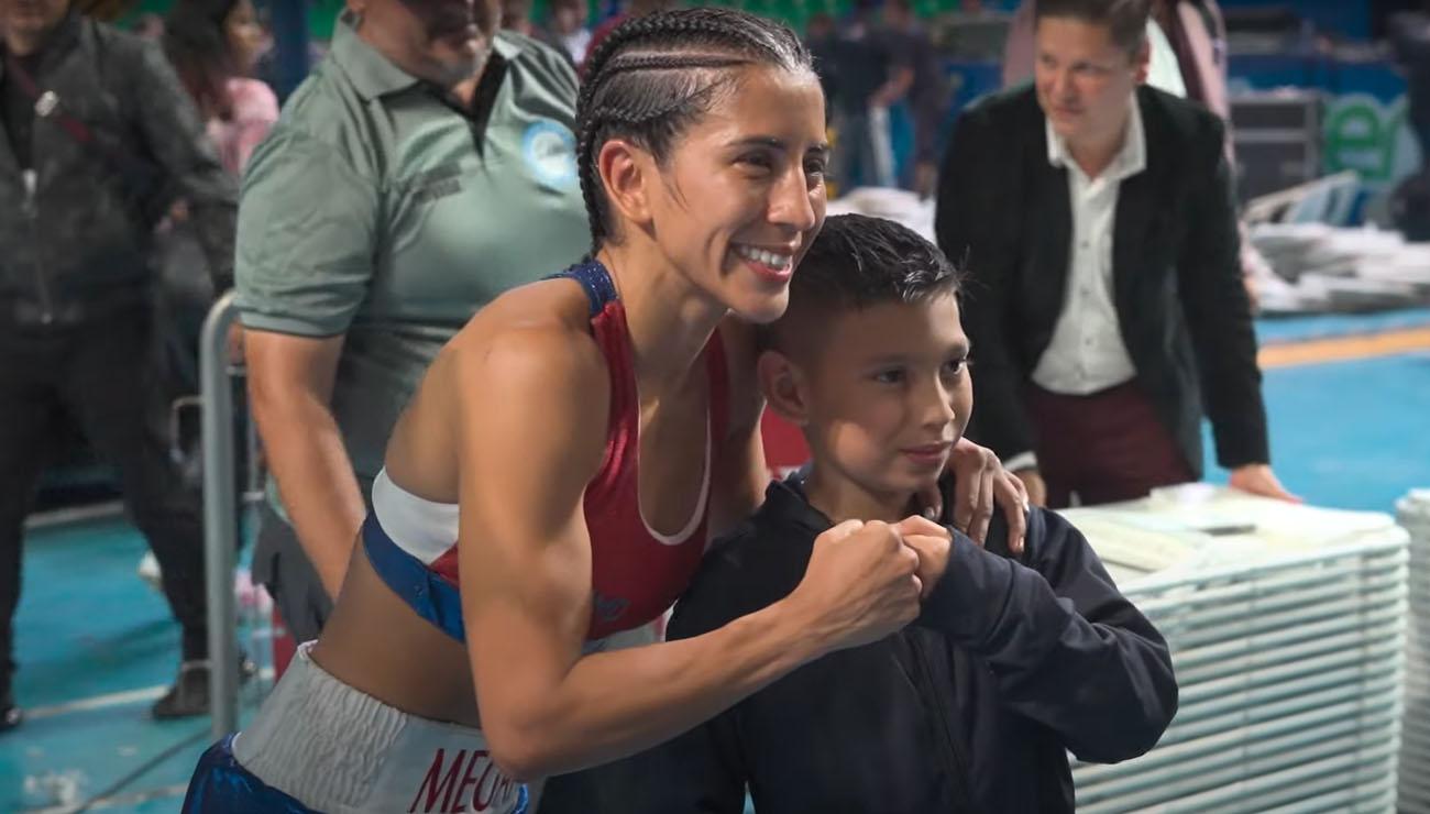 A female boxer embraces a young fan with a fist bump.