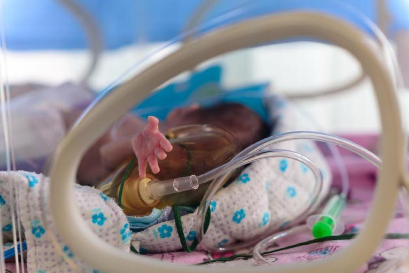 Фотография младенца, окруженного трубочками, протягивающего руку на камеру