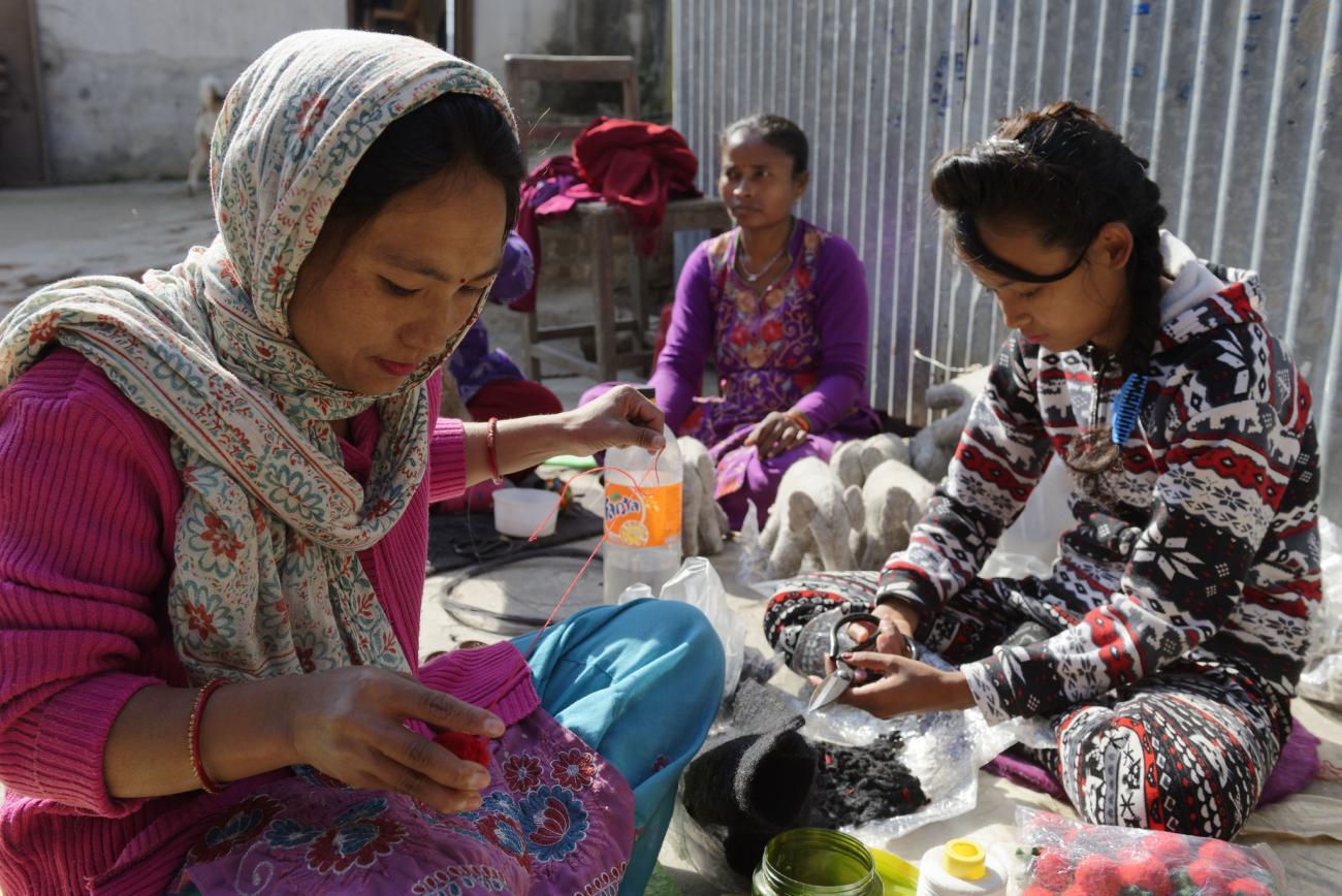 Two women in pink sweaters sew with wool