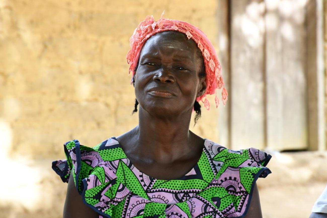 A Liberian woman in a green dress and a red headscarf in front of a window