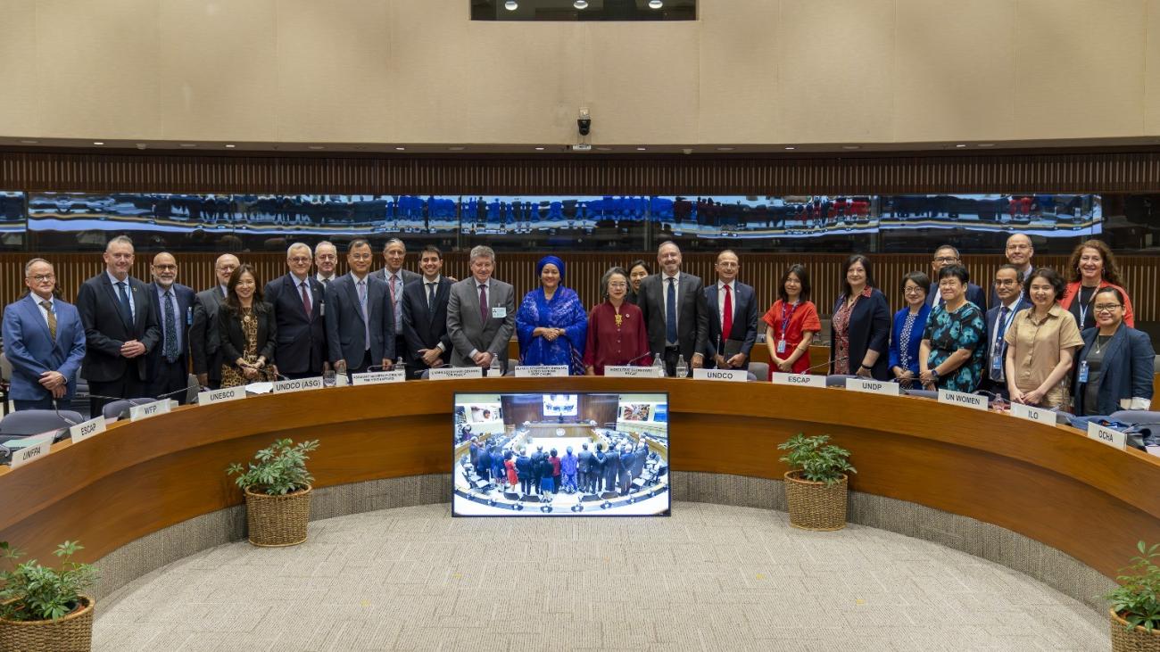 A group of UN officials stand in a semi-circle, and pose and smile for a group photo.