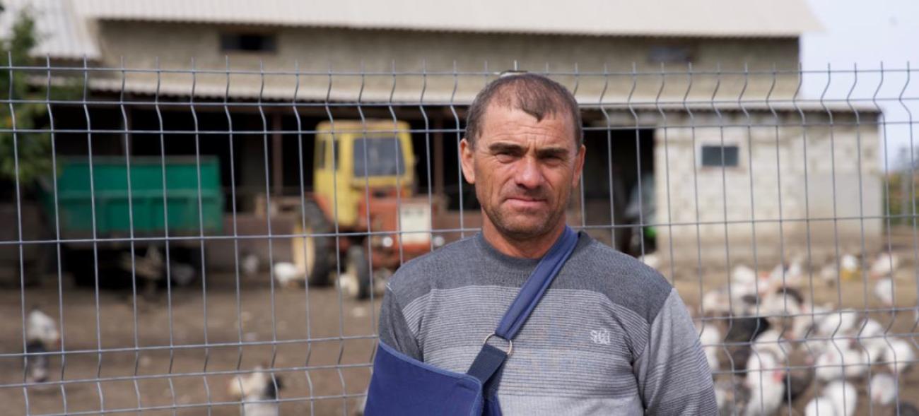 Мужчина с повязкой поддерживающей для руки стоит на фоне фермы