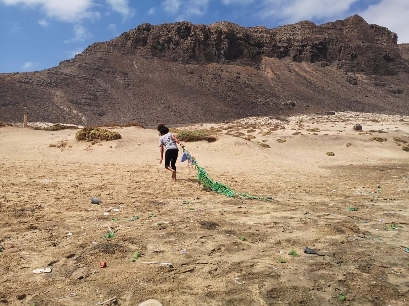 A child pulls through a green net on a sandy beach