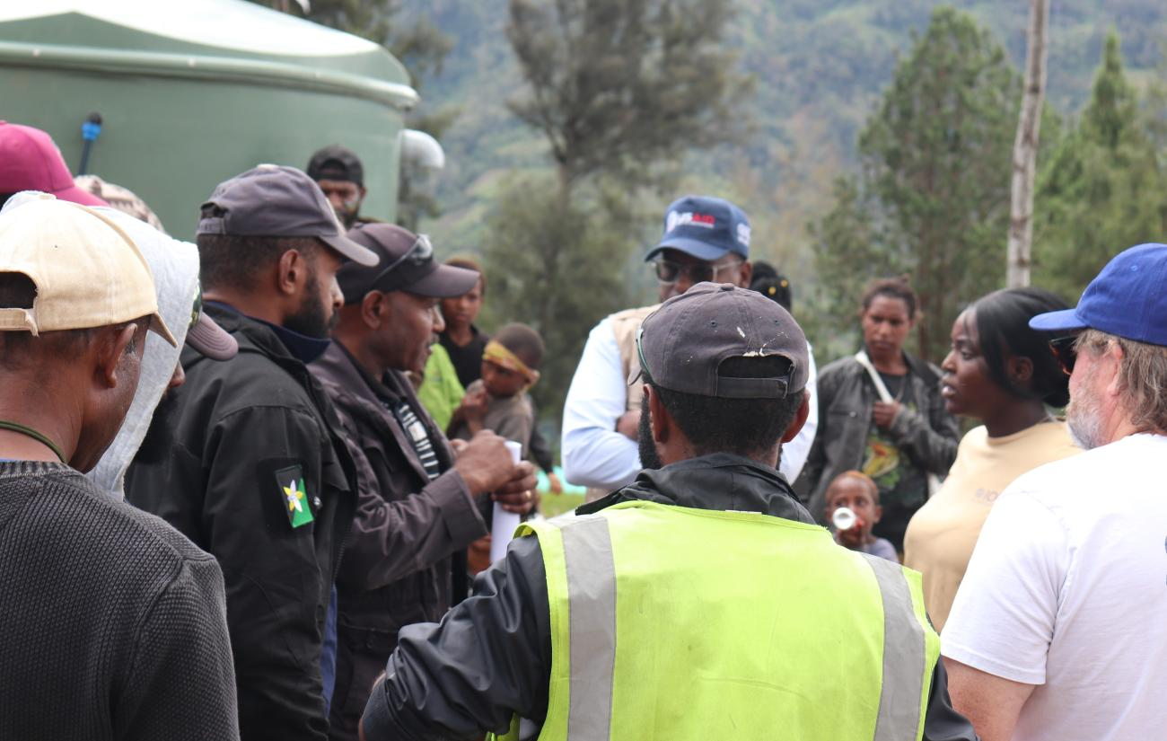A group of people gather and talk; each person dressed in dark clothes and caps, with one person in the middle in a neon coloured jacket.