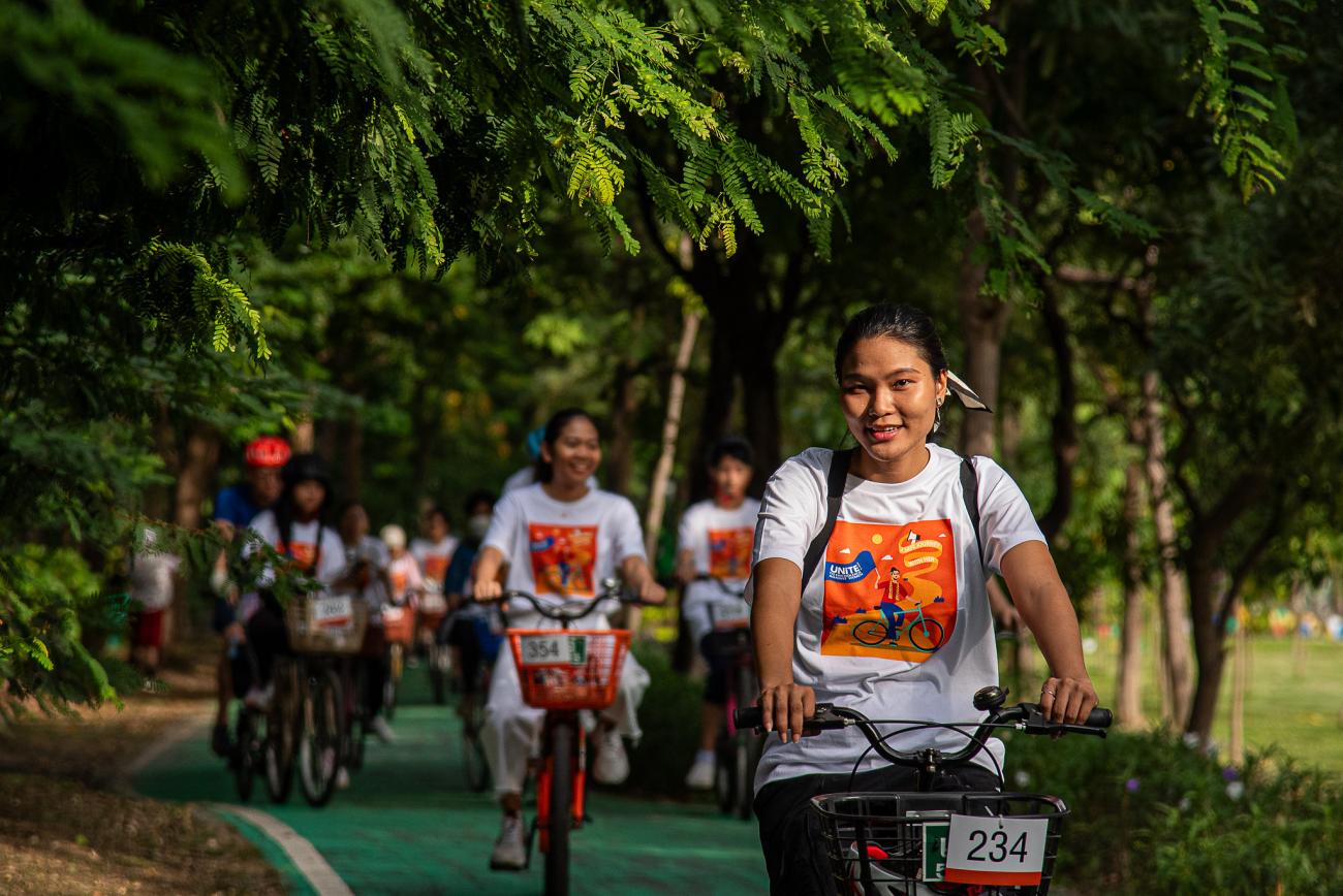 Girls in white shirts bicycling through a green wooded area