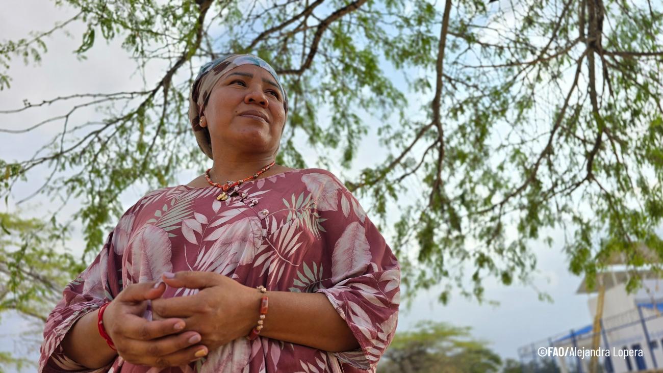 Женщина в красном платье смотрит в сторону, стоя на фоне веток дерева, покрытых листьями