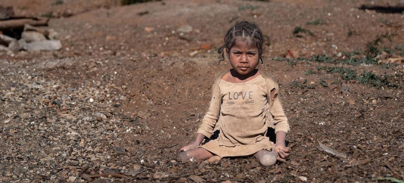 一个小女孩穿着破烂的衣服坐在一片贫瘠的土地上。