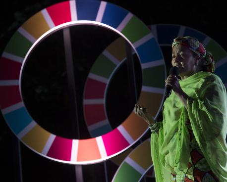 The Deputy Secretary-General on stage speaks into a microphone while standing by large SDG wheel cutouts in the background.