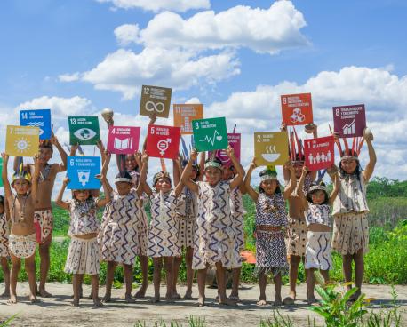 A group of children in traditional clothing carry boards with the sustainable development goals
