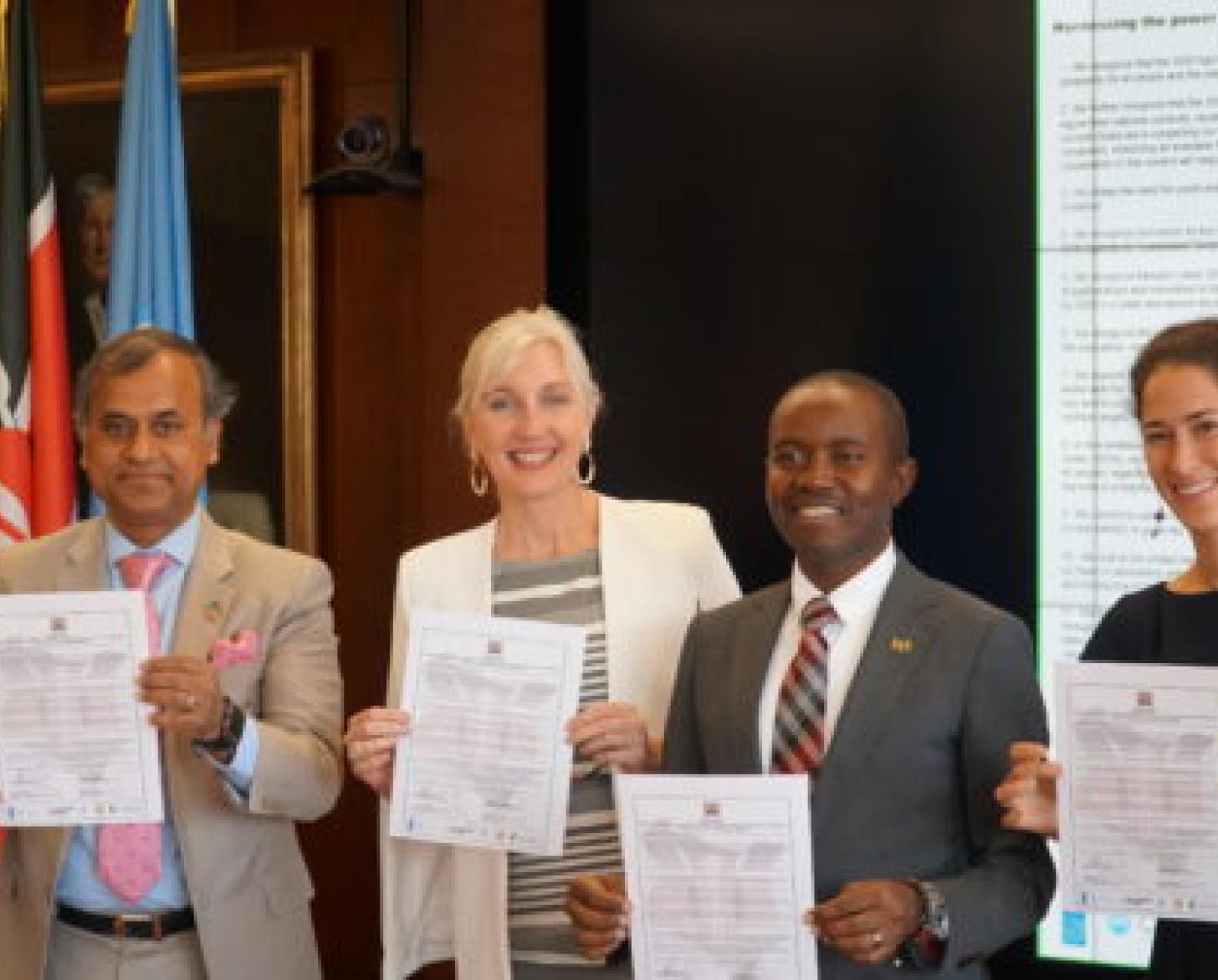 Cuatro personas paradas una al lado de la otra y cada una muestra un documento a la cámara.