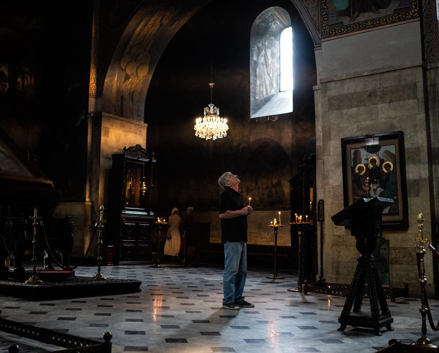 A man looks up, holding a candle, in a solemn place of worship