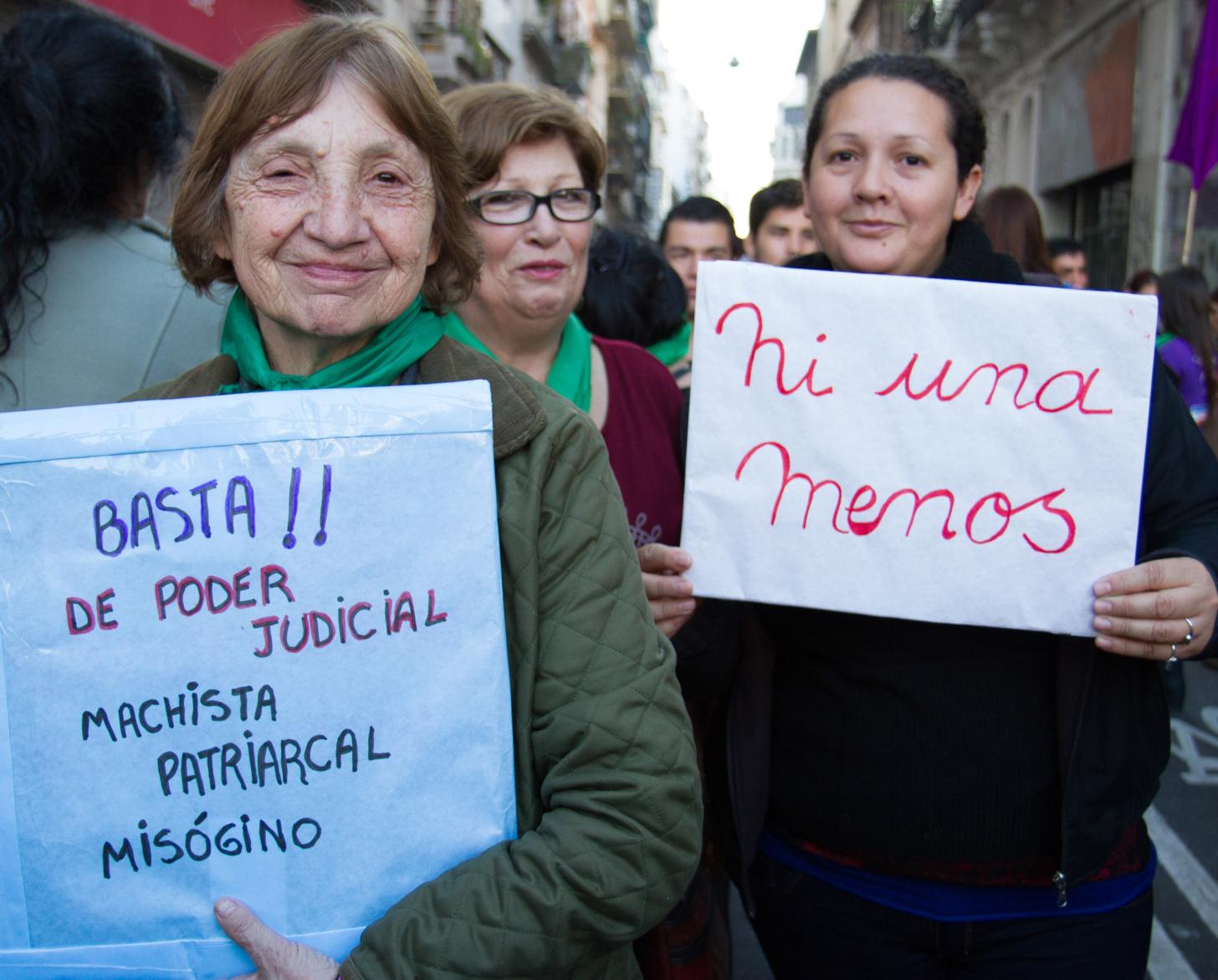 Dos manifestantes sostienen carteles, sonriendo para la cámara.