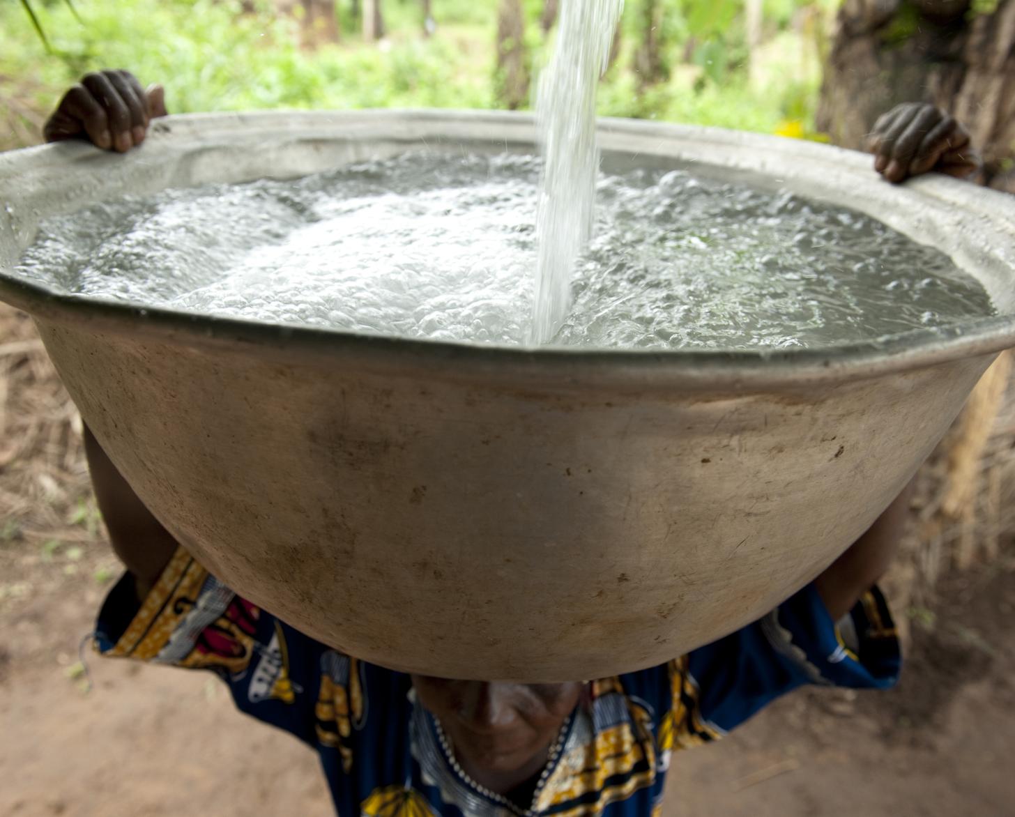 امرأة تحمل وعاءً معدنيًا كبيرًا على رأسها.