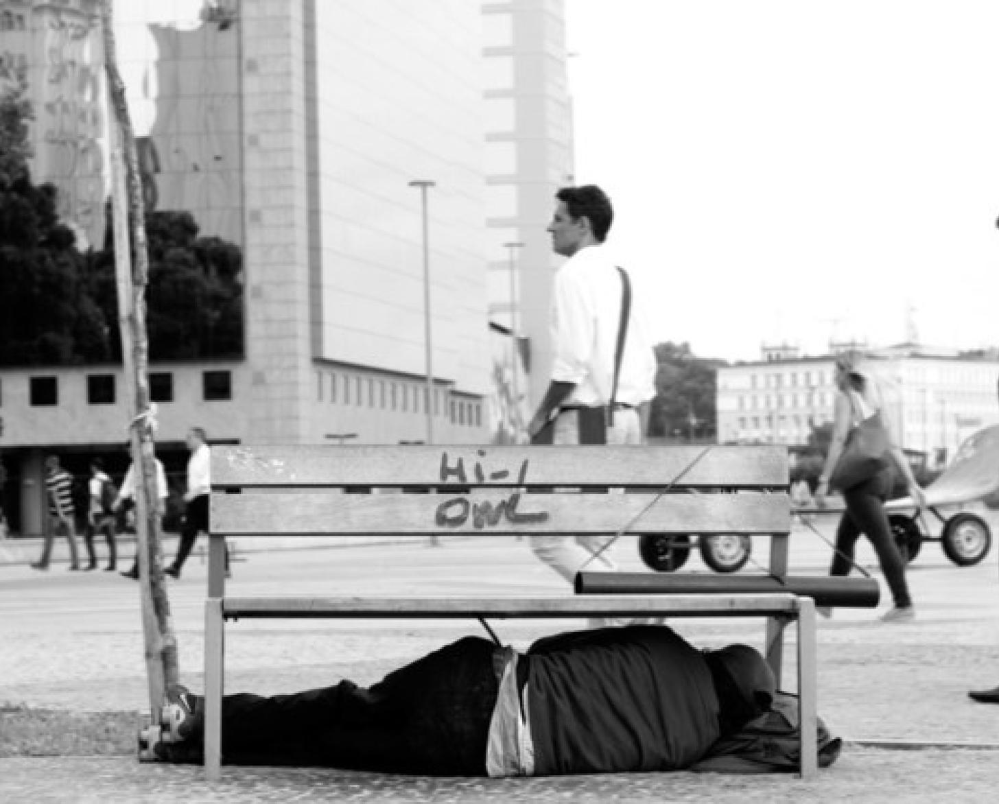 A homeless person sleeps in the streets under a bench in Rio.