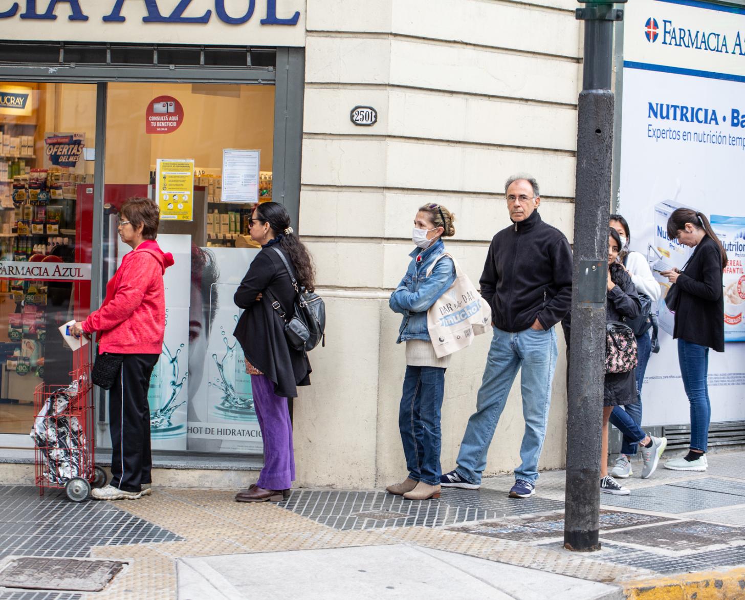 Personas esperan en una fila, frente a una farmacia en Argentina.