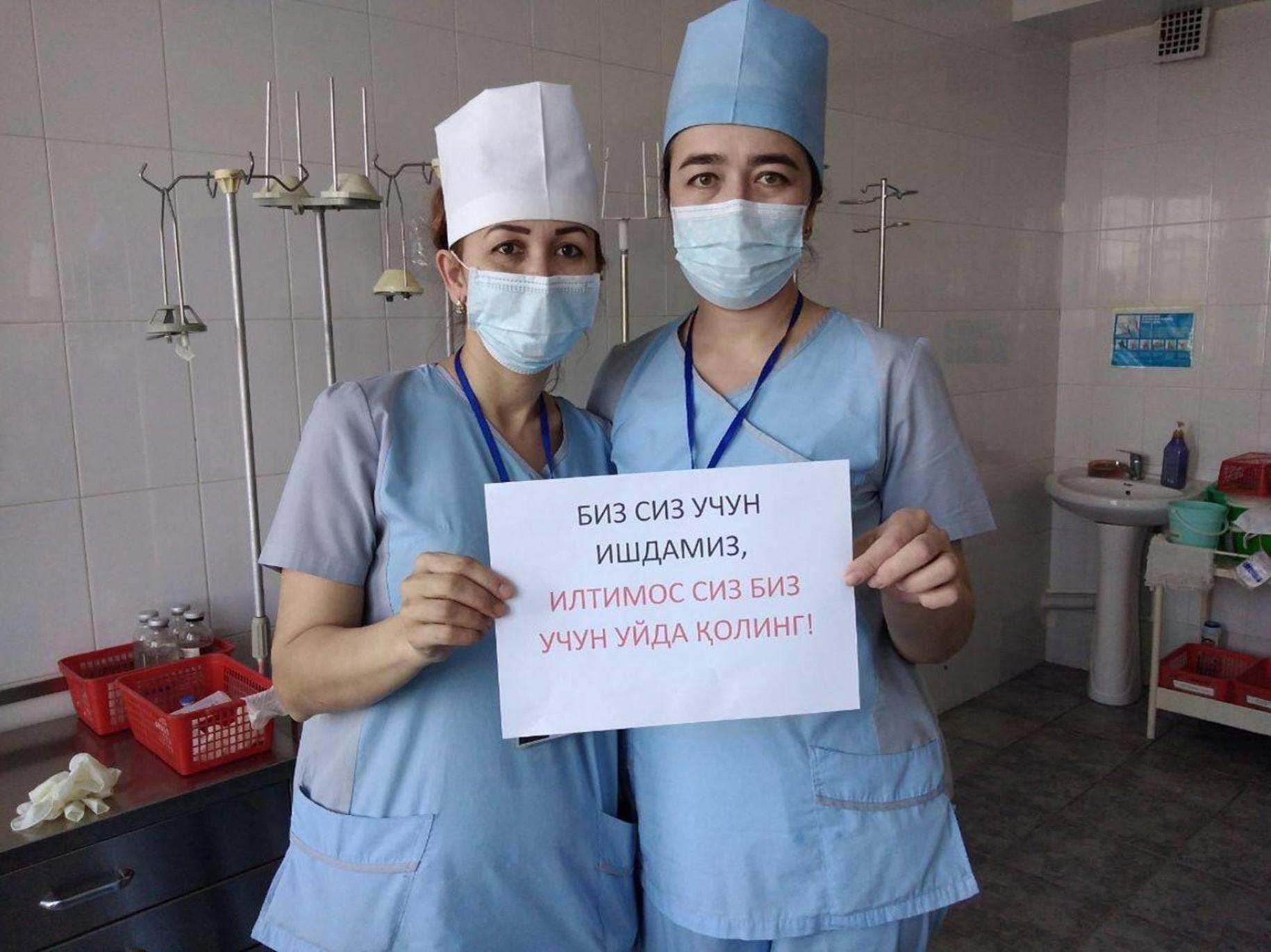 Two nurses hold up signs urging the public to stay home and safe.