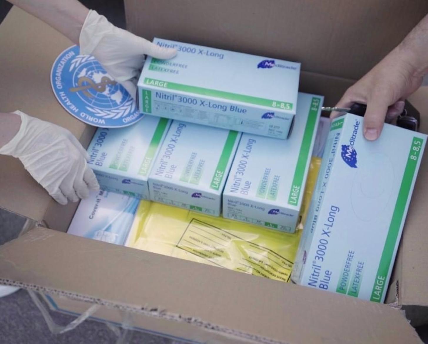 La foto muestra un primer plano de unas manos que sacan suministros para salvar vidas de una caja donada por la Organización Mundial de la Salud.