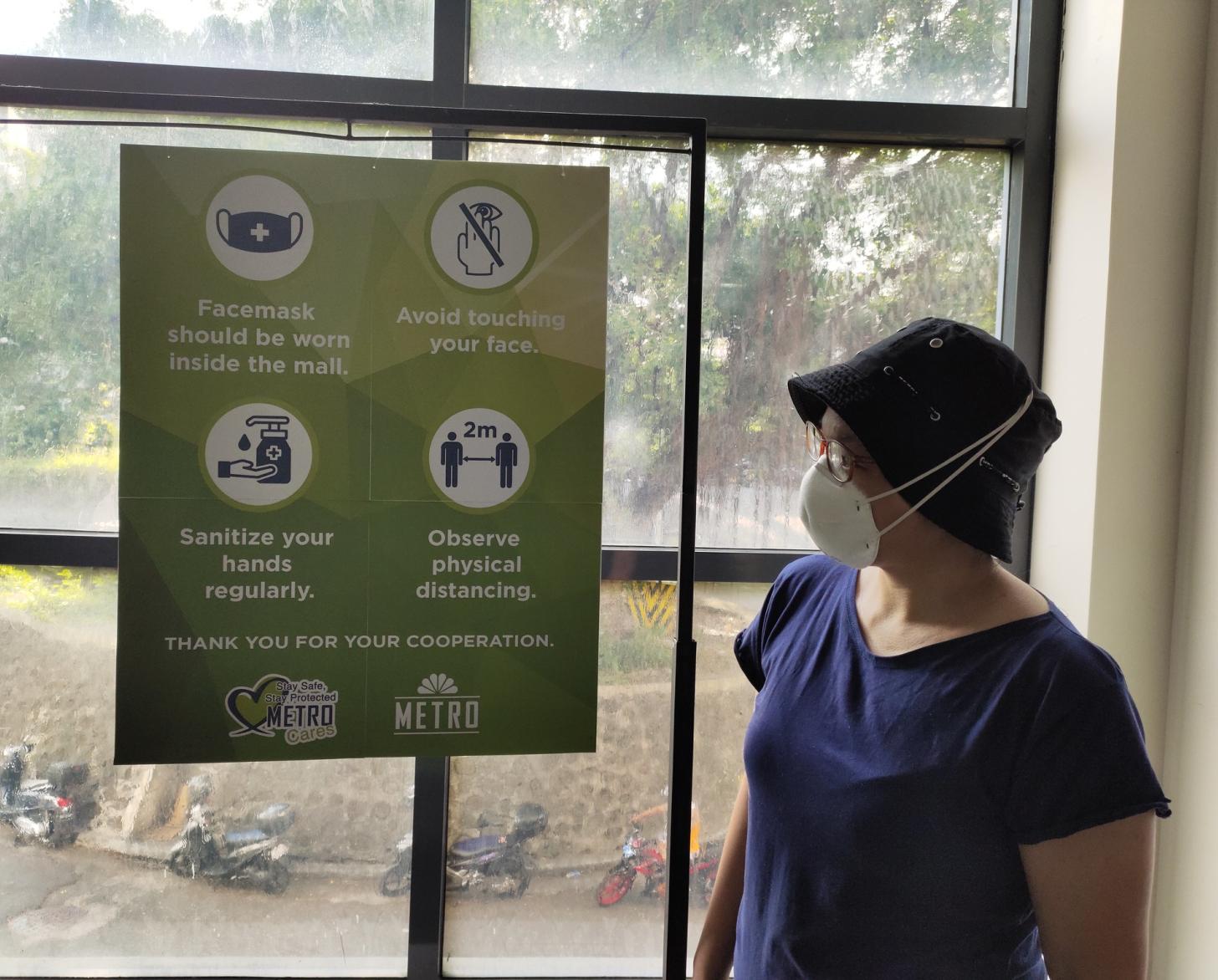 A woman stands near an awareness raising sign about safety precautions citizens should take to prevent them from catching COVID-19.