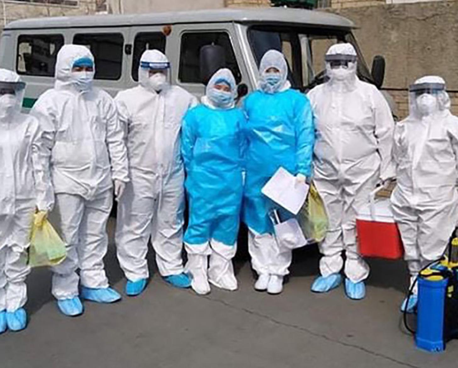 Des femmes et homme se tiennent les uns à côté des autres , face caméra, devant une camionnette. Ils portent chacun un équipement de protection individuelle de la tête aux pieds.