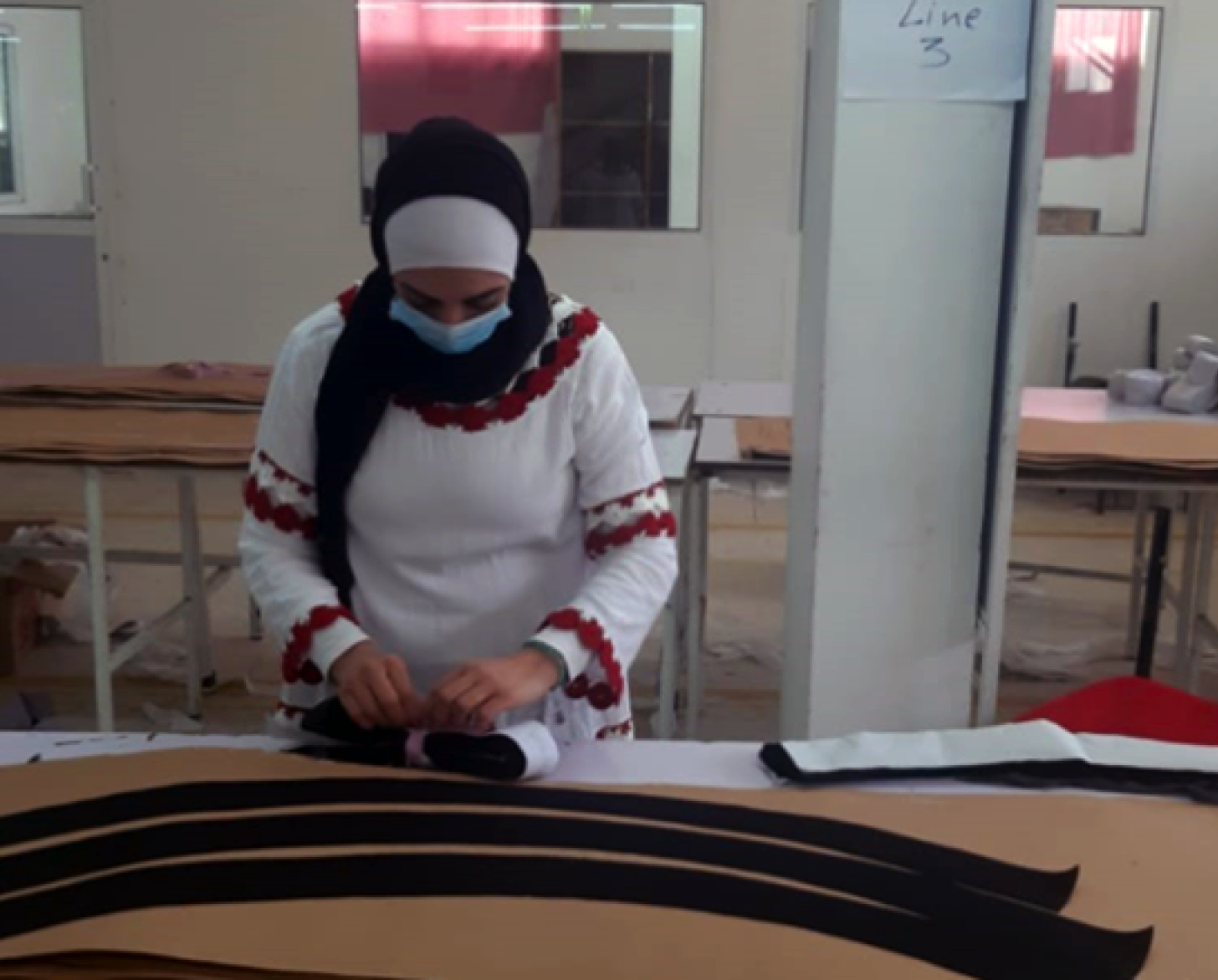 A woman wearing a protective face mask concentrates on a garment in a manufacturing space.