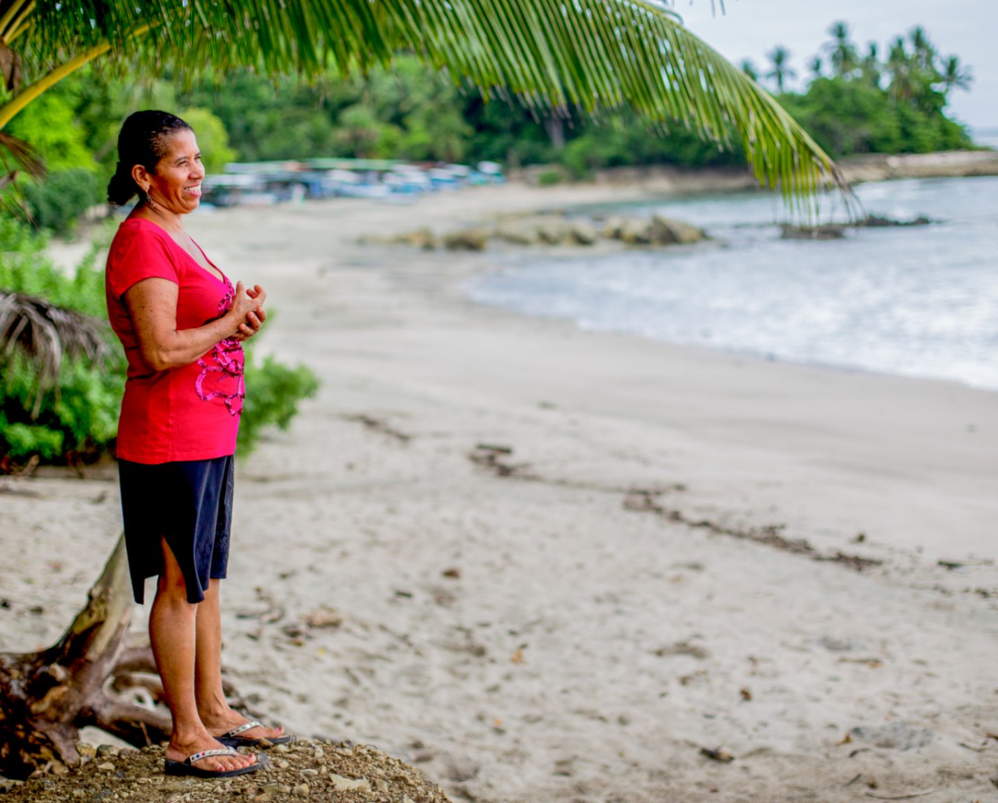 Woman smiles as she pensively as she stands on a beach looking towards the ocean. 