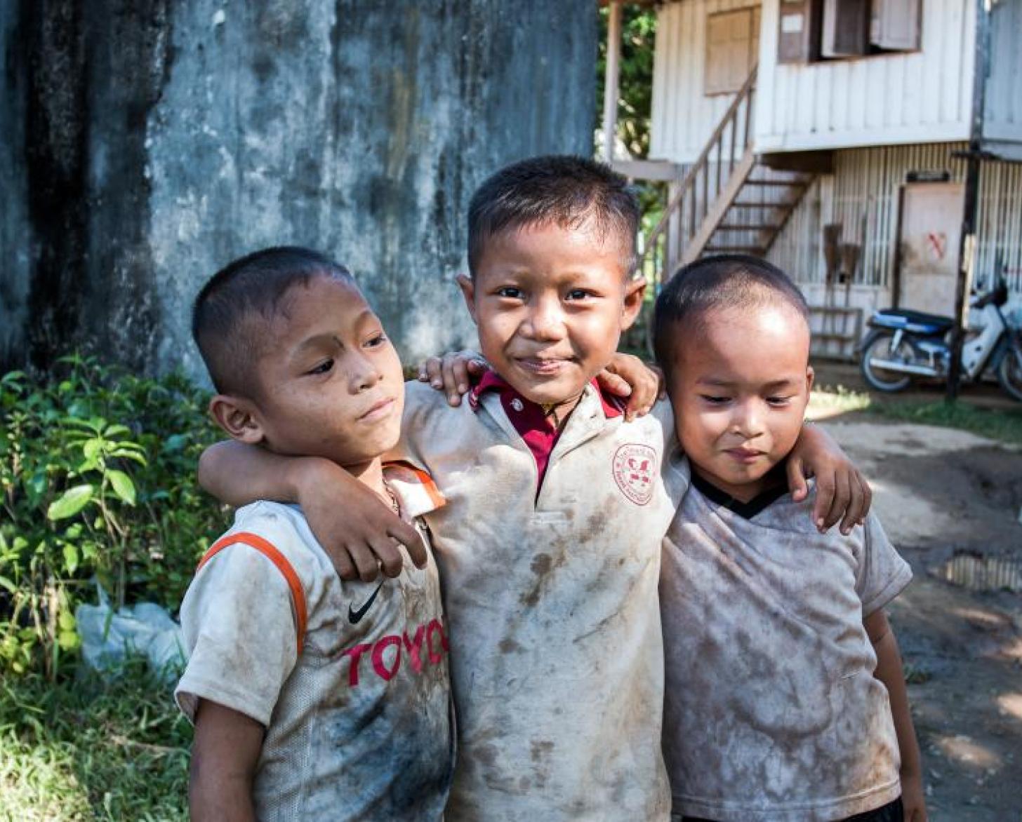 Tres niños pequeños con los brazos cruzados posan para la cámara.