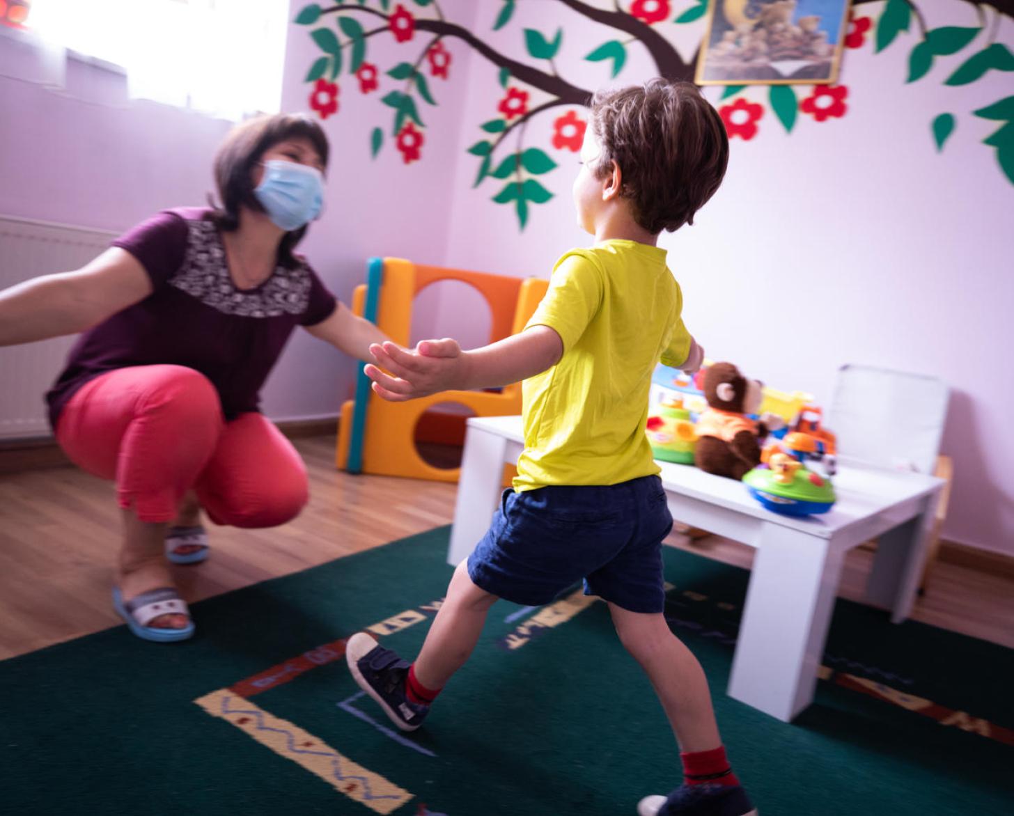 A caregiving wearing a protective face masks prepares to give a social distanced hug to one of the young residents of the programme.