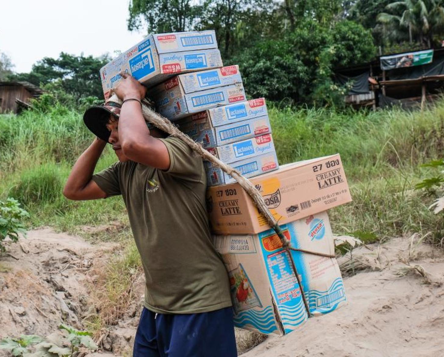 Un trabajador migrante en Tailandia lleva cajas a la espalda utilizando una cuerda para mantenerlas todas juntas.