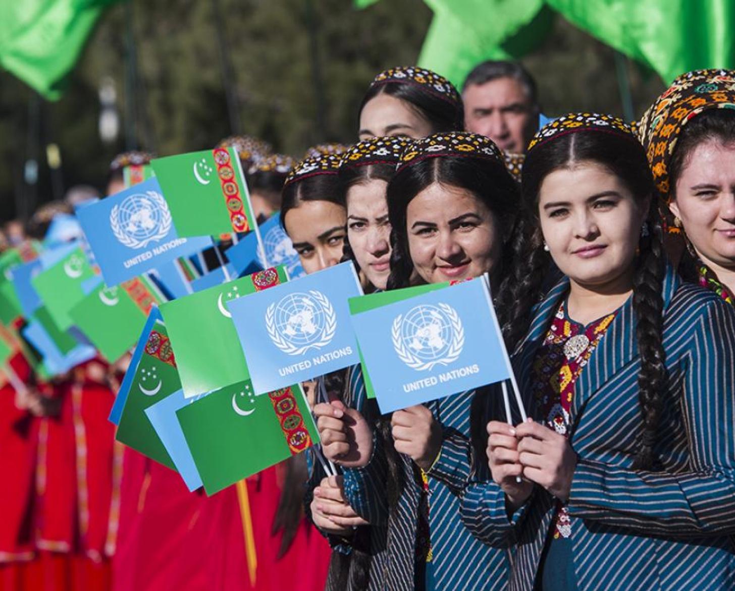 Unas jóvenes sostienen las banderas de la ONU y de Turkmenistán mientras celebran la inauguración de la Casa de la ONU.