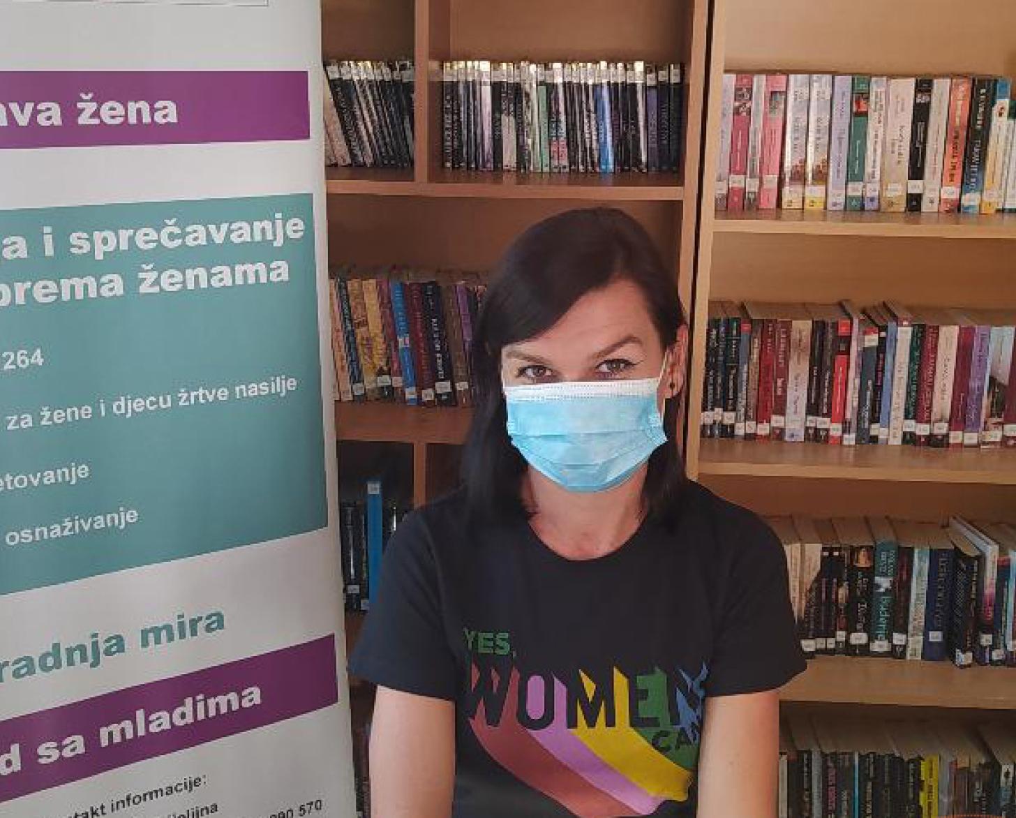Dragana Petric se sienta frente a una estantería de libros y una señalización en la Fundación Lara Bijeljina.
