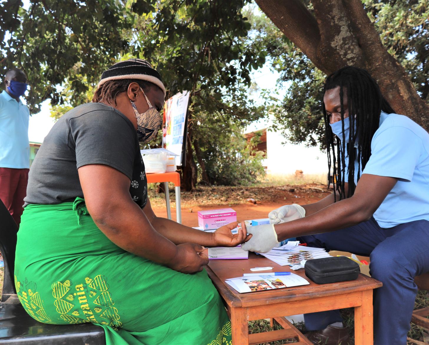 Un trabajador sanitario atiende a una mujer en un puesto de trabajo en el exterior mientras un hombre espera su turno.