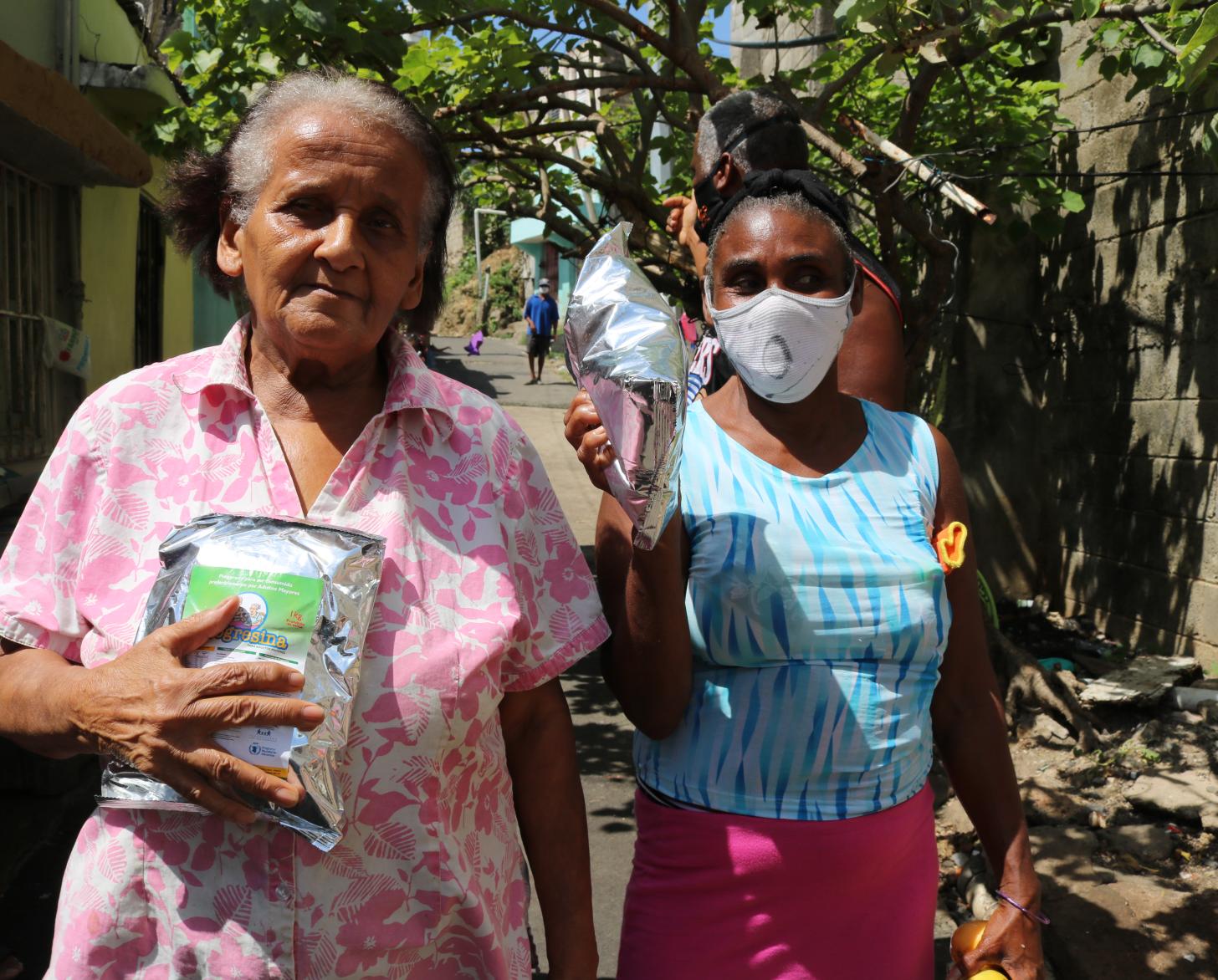 Dos mujeres sostienen de forma destacada los suministros de alimentos recibidos del Programa Mundial de Alimentos.