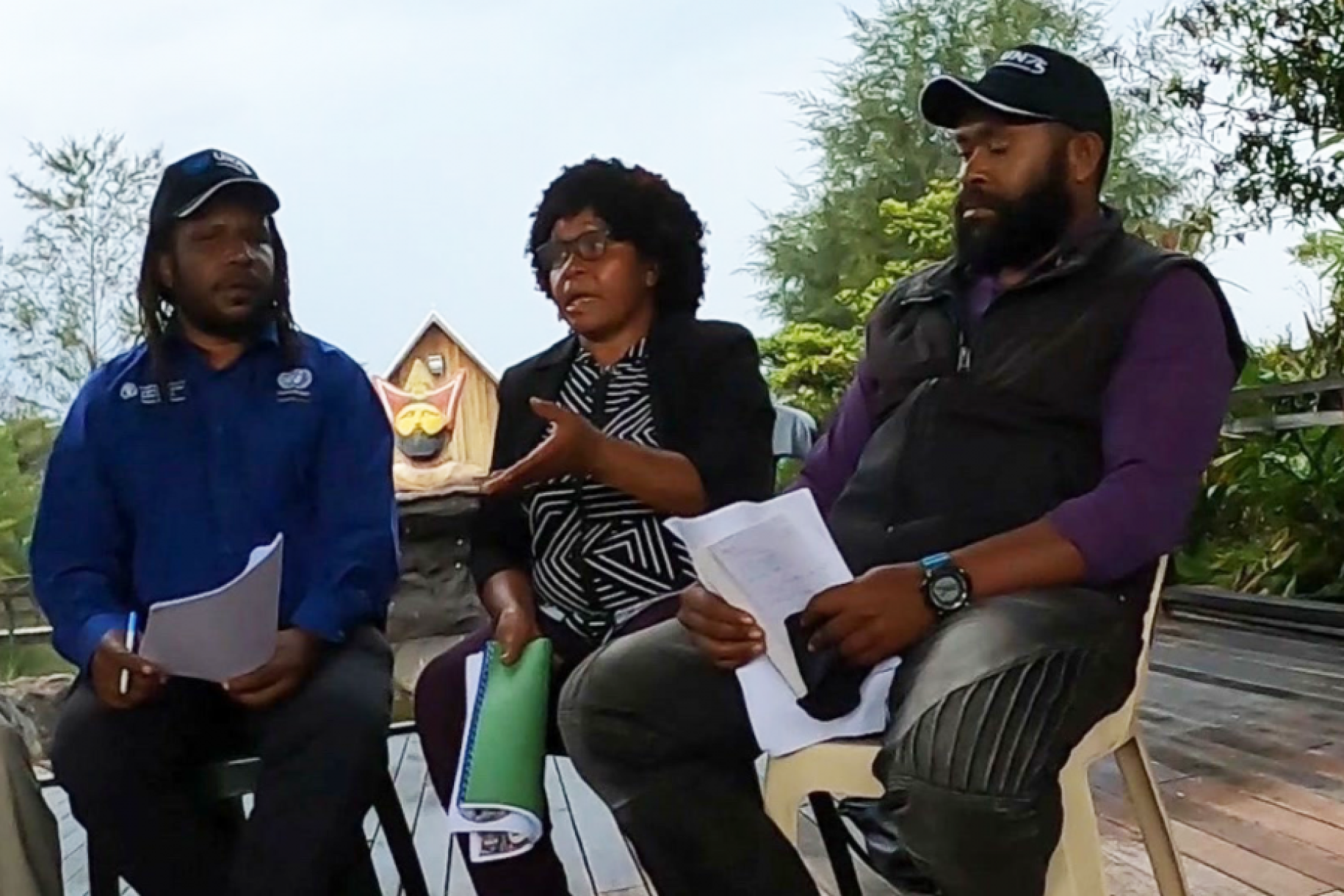 Mary Tamia se sienta entre dos hombres mientras habla de la construcción de la paz durante una mesa redonda en Tari, provincia de Hela.