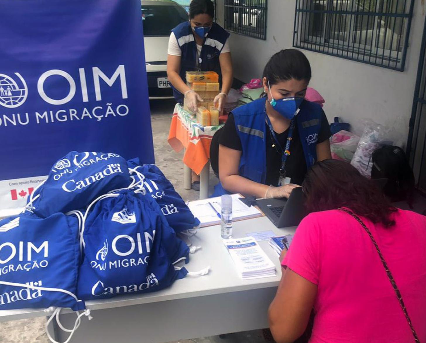 IOM staff at a distribution facility sit with a recipient of a hygiene kit. 